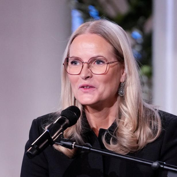 Mette-Marit mit Brille spricht in ein Mikrofon.