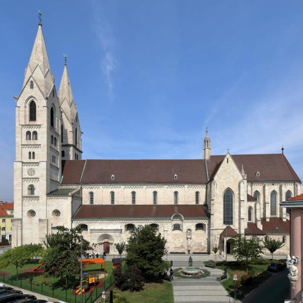 Große Kirche mit zwei hohen Türmen, rotem Dach und Spielplatz im Vordergrund an einem sonnigen Tag.