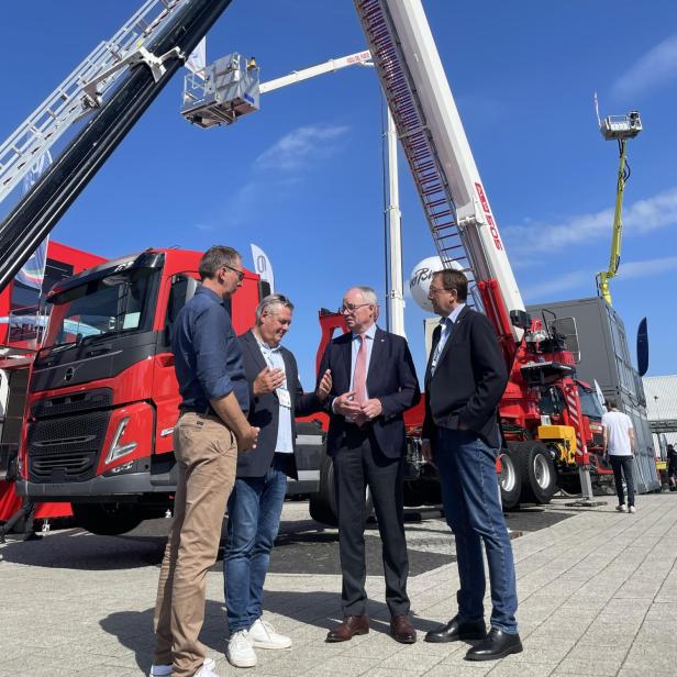 Vier Männer im Gespräch vor modernen Feuerwehrfahrzeugen mit ausfahrbaren Drehleitern auf der Interschutz-Messe in Hannover.