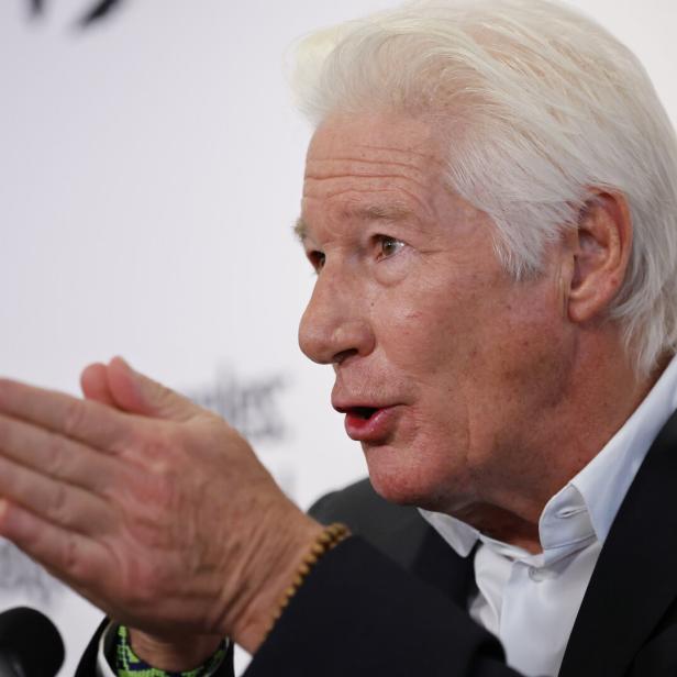 Richard Gere mit grauem Haar gestikuliert und schaut zur Seite.