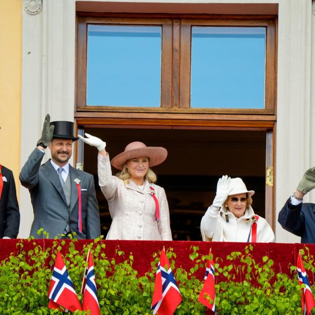 Die norwegische Königsfamilie winkt elegant gekleidet von einem Balkon.
