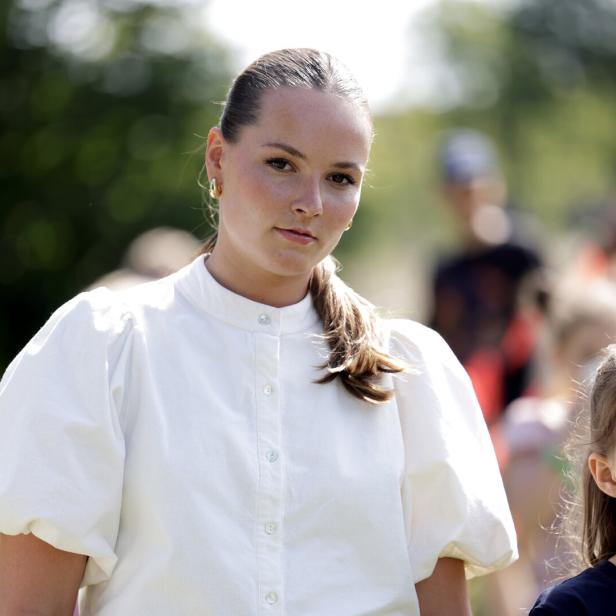 Prinzessin Ingrid Alexandra mit weißer Bluse und ein Mädchen stehen im Freien, im Hintergrund sind weitere Menschen unscharf zu sehen.