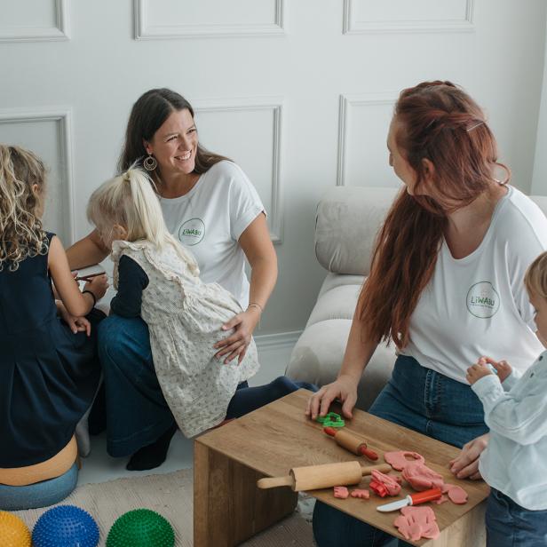 Zwei Betreuerinnen spielen und basteln mit mehreren Kindern in einem hellen Raum.