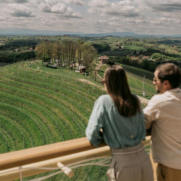 Ein Paar genießt von einer Terrasse aus den weiten Blick über grüne Hügel und Weinberge in einer ländlichen Region Kroatiens.