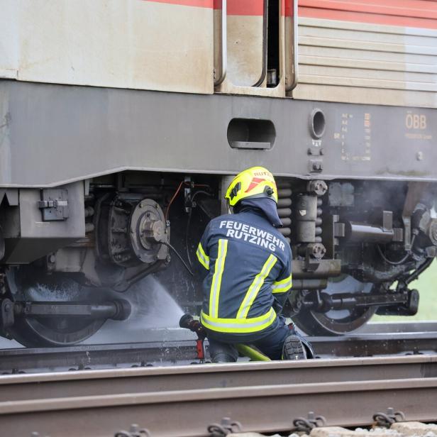 Ein Feuerwehrmann löscht mit einem Schlauch einen Brand am Fahrwerk eines Zuges auf den Gleisen.