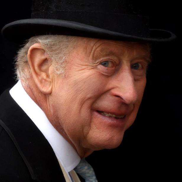 König Charles III. trägt einen schwarzen Hut und einen Anzug vor einem dunklen Hintergrund.