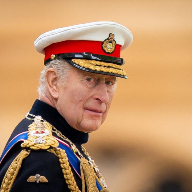 König Charles III. trägt eine militärische Uniform mit einer weißen Schirmmütze und goldenen Abzeichen vor einem hellen Hintergrund.