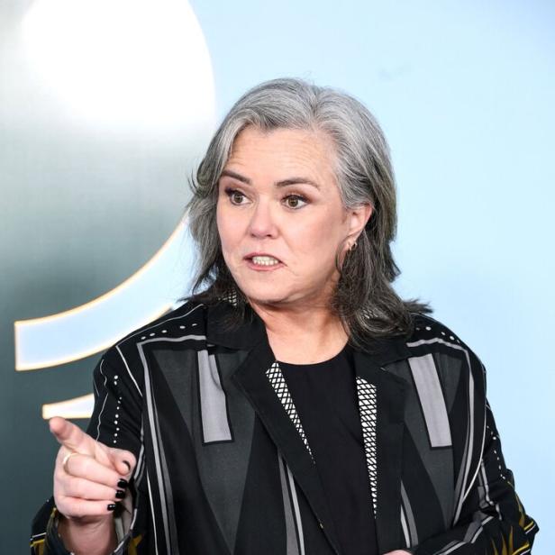 Rosie O’Donnell mit grauem Haar trägt einen gemusterten Blazer und zeigt mit dem Finger nach vorne.