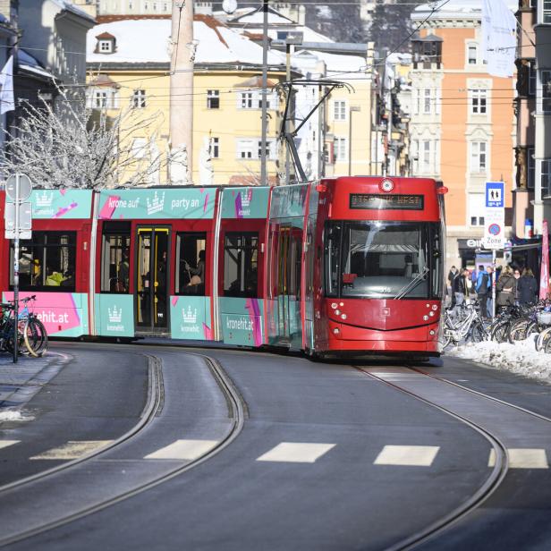 Eine rot-türkise Straßenbahn fährt durch eine winterliche Stadtstraße mit vielen geparkten Fahrrädern und Fußgängern am Rand.
