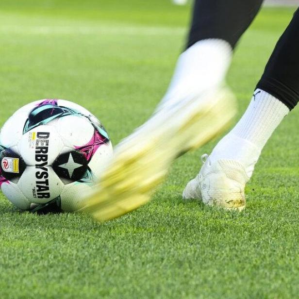 Ein Fußballspieler mit weißen Schuhen schießt einen Ball auf grünem Rasen.