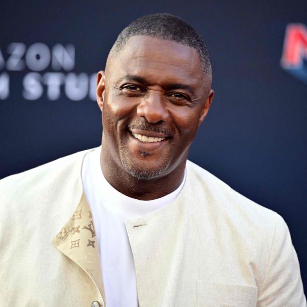 Idris Elba lächelt vor einem Hintergrund von Amazon MGM Studios in die Kamera.