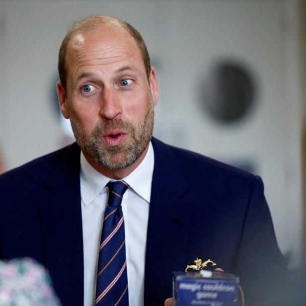 Prinz William trägt einen dunkelblauen Anzug mit Krawatte und spricht in einem Gespräch mit anderen Personen.