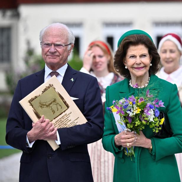 König Carl XVI. Gustaf und Königin Silvia von Schweden bei einem öffentlichen Auftritt, wobei die Königin einen Blumenstrauß hält.