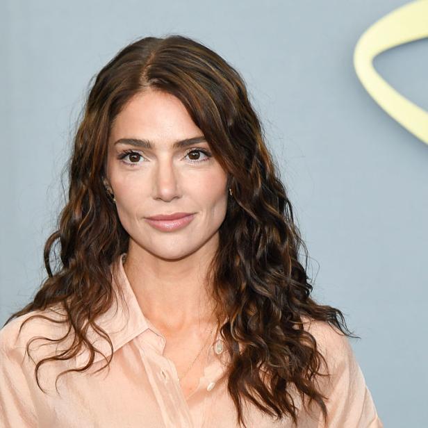 Janet Montgomery lächelt in pfirsichfarbener Bluse vor hellblauem Hintergund.