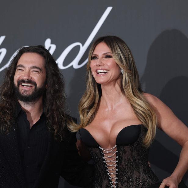 Heidi Klum und Tom Kaulitz lachen gemeinsam vor einem Chopard-Hintergrund in die Kamera.