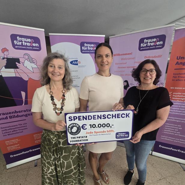Drei Frauen halten einen Spendenscheck über 10.000 Euro vor Infotafeln von Frauen für Frauen.