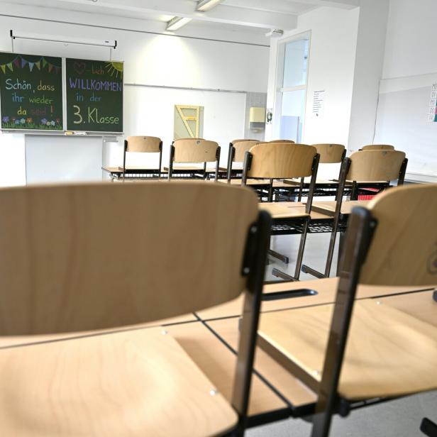 Leerer Klassenraum mit hochgestellten Stühlen und einer Tafel, auf der eine Willkommensbotschaft für die 3. Klasse steht.