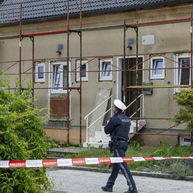 Ein Polizist steht vor einem mit Absperrband gesicherten Haus, das von Baugerüsten umgeben ist.
