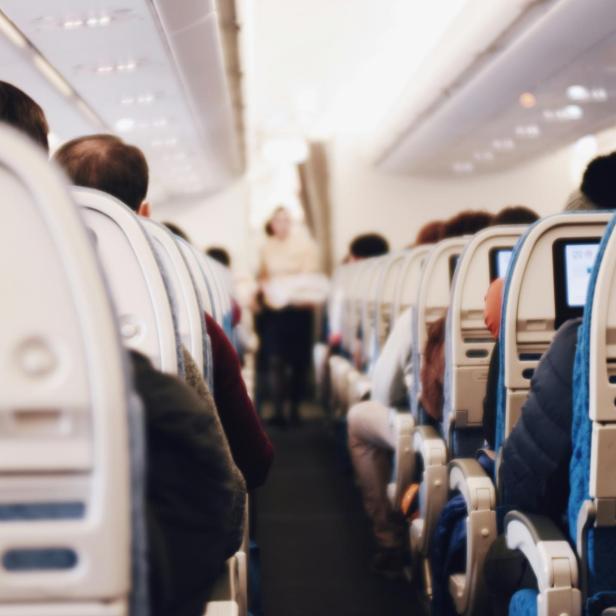 Flugzeugkabine mit Passagieren in den Sitzreihen und einer Flugbegleiterin im Gang.