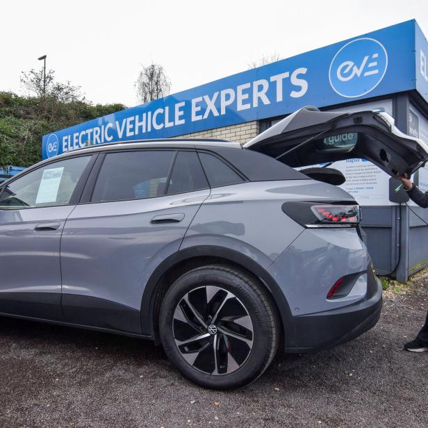 Frau öffnet Kofferraum eines Elektroautos bei einem Gebrauchtwagenhändler.
