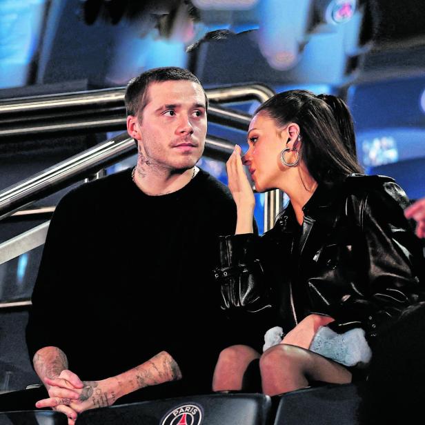 Brooklyn Beckham und Nicola Peltz sitzen nebeneinander auf der Tribüne eines Stadions und unterhalten sich.