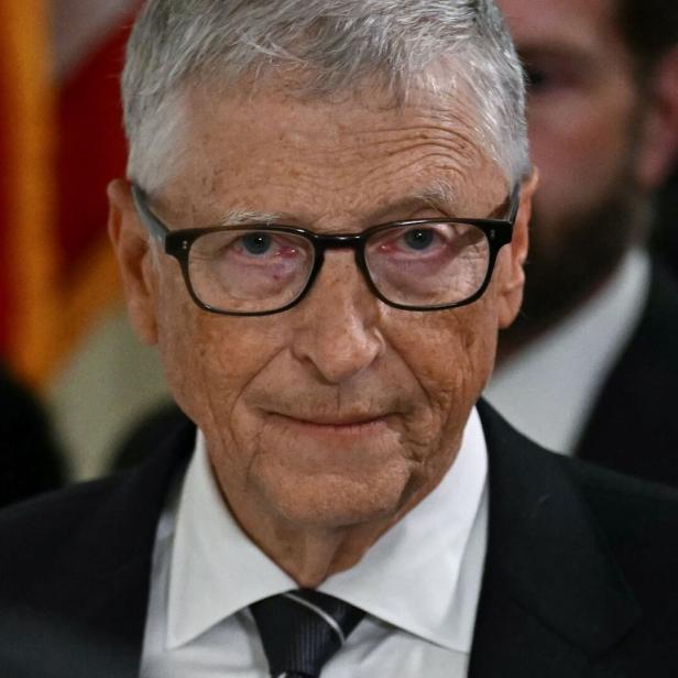 Bill Gates trägt eine Brille, ein weißes Hemd sowie einen dunklen Anzug und blickt ernst in die Kamera.