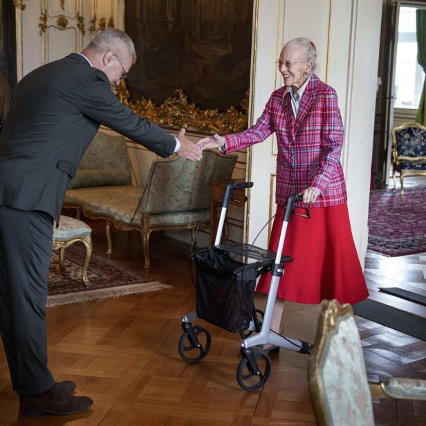Königin Margrethe II. von Dänemark begrüßt einen Mann mit Handschlag, während sie sich auf einen Rollator stützt.
