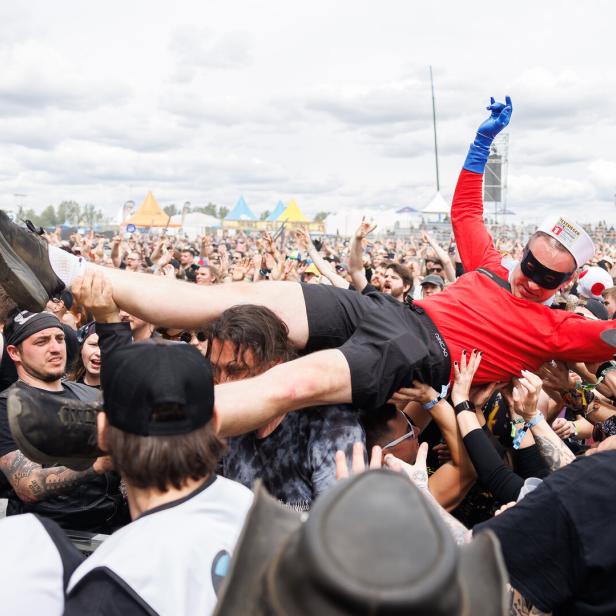 Eine verkleidete Person wird beim Crowdsurfing von einer großen, feiernden Menschenmenge getragen.