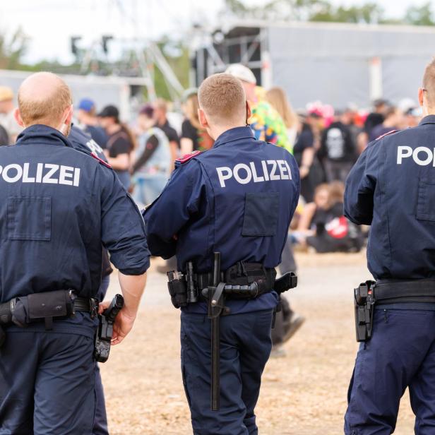 Mehrere Polizisten stehen mit dem Rücken zur Kamera vor einer Menschenmenge bei einer Veranstaltung.