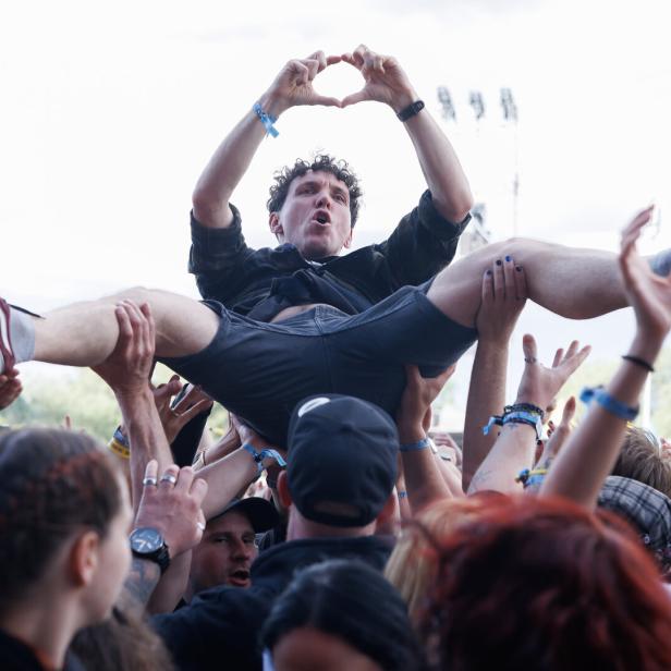Eine Menschenmenge trägt eine Person beim Crowdsurfing, die mit den Händen ein Herz formt.