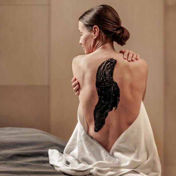 Eine Frau mit hochgesteckten Haaren sitzt mit einem weißen Handtuch und schwarzer Maske auf dem Rücken.