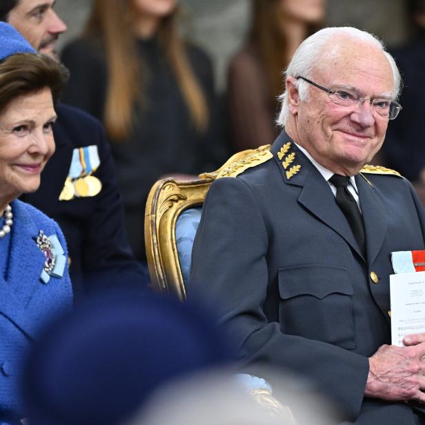 König Carl XVI. Gustaf und Königin Silvia von Schweden sitzen bei einer offiziellen Veranstaltung in festlicher Kleidung nebeneinander.