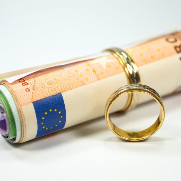 Zusammengerollte Eurobanknoten mit zwei goldenen Ringen auf weißem Hintergrund.