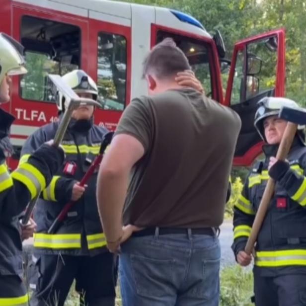 Drei Feuerwehrleute in Uniform sprechen mit einem Mann vor einem Einsatzfahrzeug im Grünen.