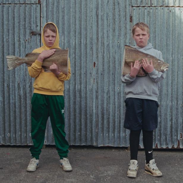 Zwei isländische Buben halten jeweils einen Fisch und schauen in die Kamera.