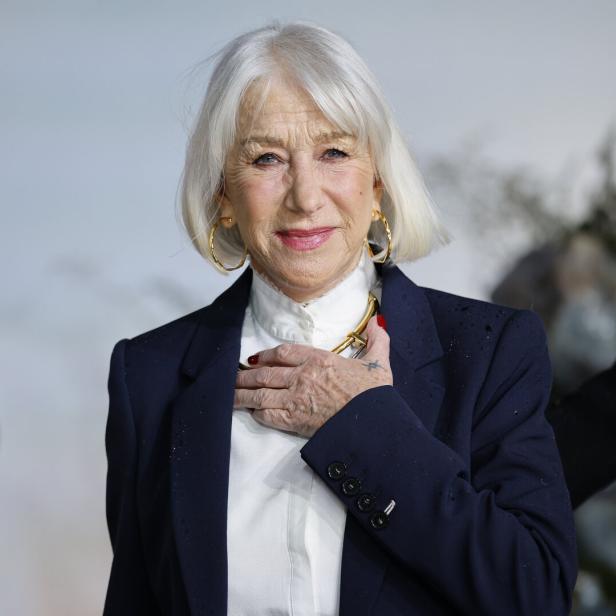 Helen Mirren trägt einen dunkelblauen Blazer über einer weißen Bluse und lächelt in die Kamera.