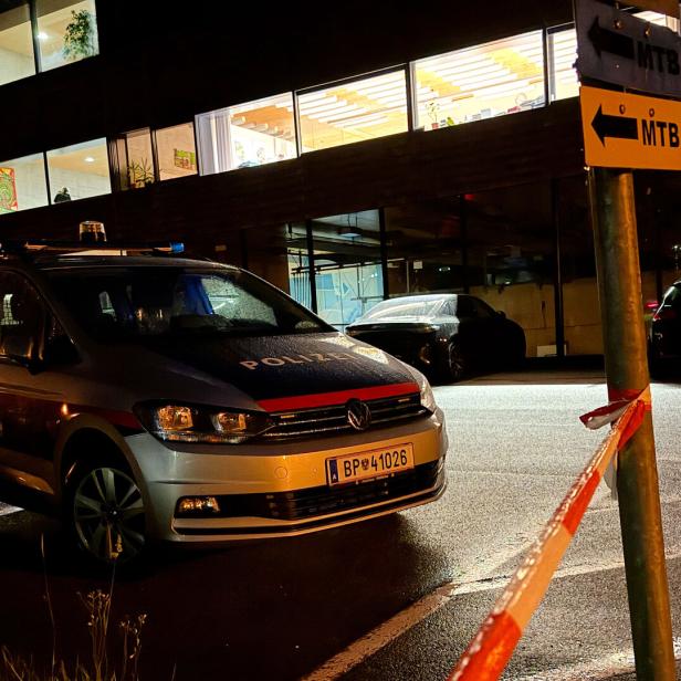 Ein österreichischer Polizeiwagen steht nachts vor einem beleuchteten Gebäude, abgesperrt durch ein rot-weißes Absperrband.