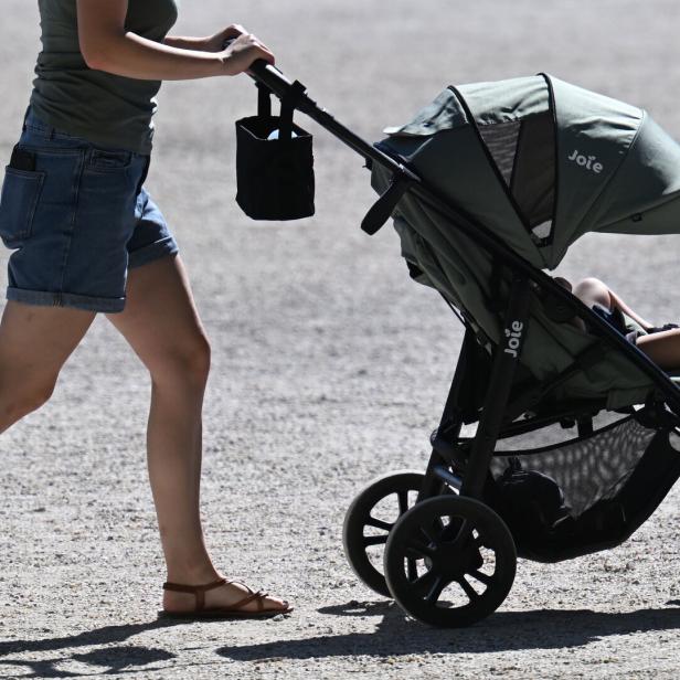 Eine Person schiebt einen Kinderwagen mit einem sitzenden Kind auf einem sonnigen Weg.