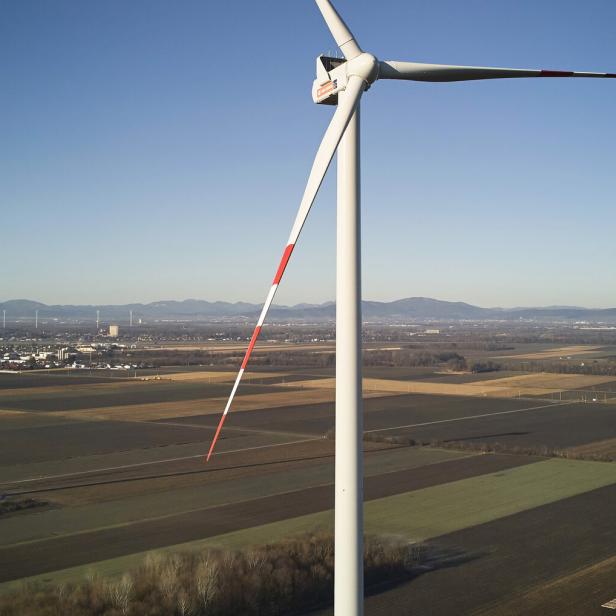 Mehrere Windkraftanlagen stehen auf weiten Feldern, eine wird gerade mit einem Kran aufgebaut, im Hintergrund Berge.