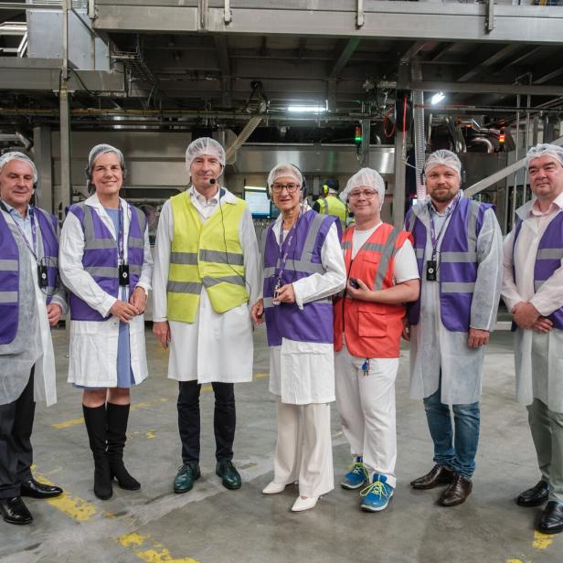 Sieben Personen mit Schutzanzügen stehen in einer Produktionshalle