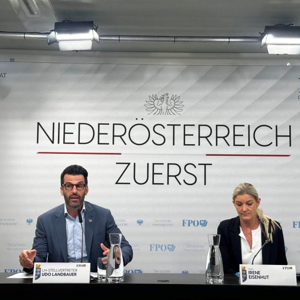 Zwei Personen sitzen an einem Tisch mit Namensschildern vor einer Wand mit der Aufschrift „Niederösterreich zuerst“.