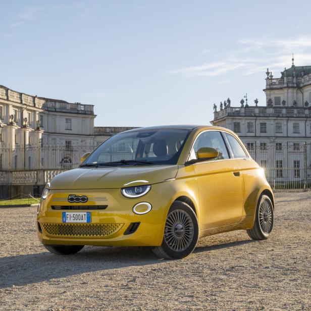 Gelber Fiat 500 vor einem historischen Schloss bei Sonnenlicht.