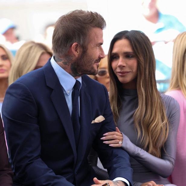 David Beckham im Anzug und Victoria Beckham in einem grauen Kleid sitzen nebeneinander, während Tom Cruise links daneben zu sehen ist.