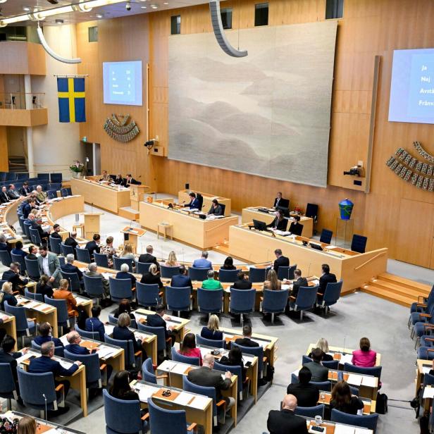 Schwedischer Reichstag mit vielen Abgeordneten bei einer Abstimmung, Ergebnis auf den Bildschirmen sichtbar.