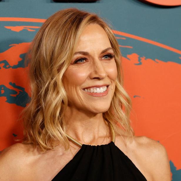 Sheryl Crow lächelt vor einem Hintergrund mit einer stilisierten Weltkarte.