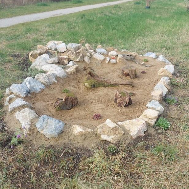 Kleines rundes Steingartenbeet mit Sandfläche und Baumstümpfen im Park.