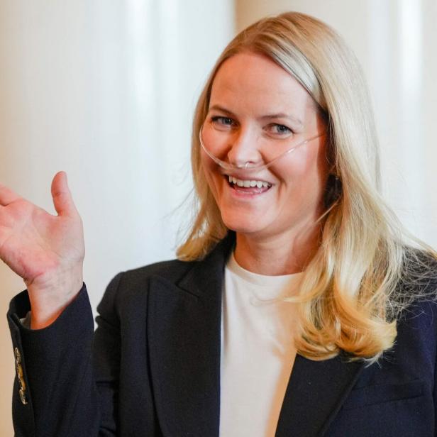 Kronprinzessin Mette-Marit von Norwegen lächelt freundlich und winkt mit der Hand, während sie eine Nasenbrille zur Sauerstoffzufuhr trägt.