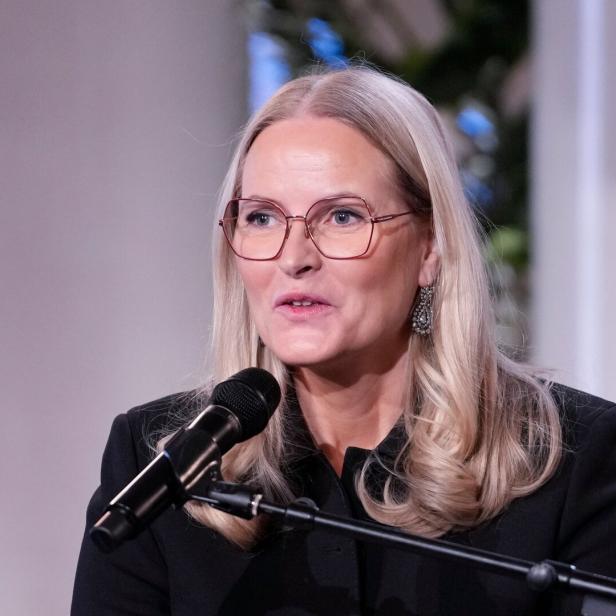 Kronprinzessin Mette-Marit von Norwegen spricht in einem schwarzen Blazer vor einem Mikrofon.