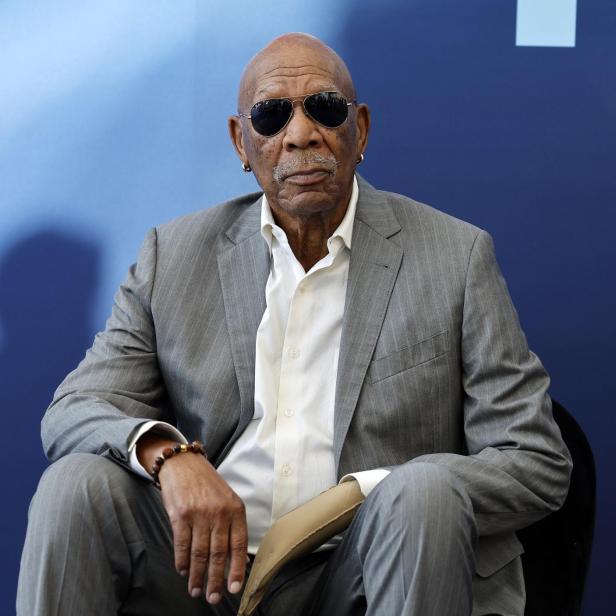 Morgan Freeman trägt einen grauen Anzug, ein weißes Hemd und eine Sonnenbrille vor einem dunkelblauen Hintergrund.