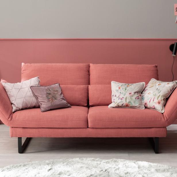Pinkes Sofa in einem kleinen, stilvoll eingerichteten Wohnzimmer mit Kissen, Wanddeko und Beistelltisch.